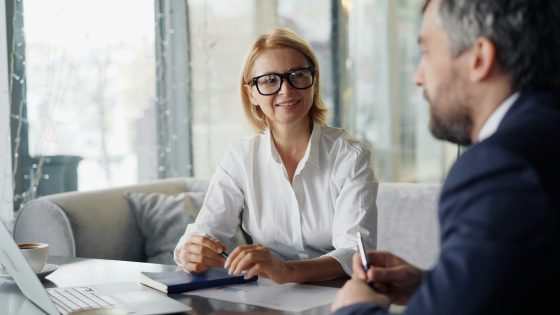 A man and woman sitting at a table with a laptop discussing business