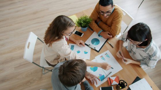 Overhead view of a diverse project team collaborating around a table, intently analyzing charts, graphs, and data reports for data-driven decision making.