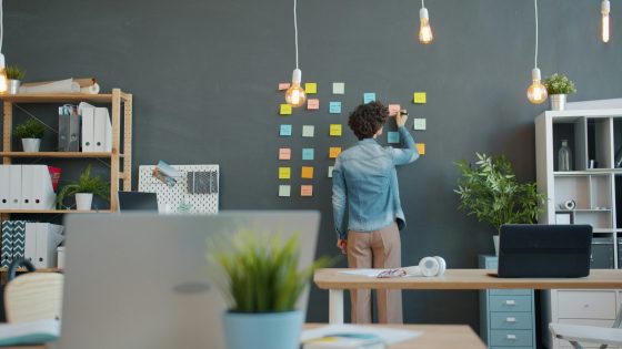 Person organizing project tasks with sticky notes on a wall in a modern office workspace